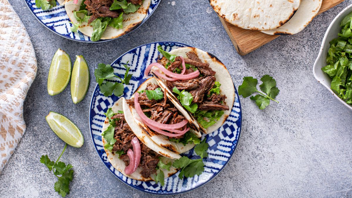 Beef tacos with chopped parsley and pickled red onions served on plate next to three slices of lime