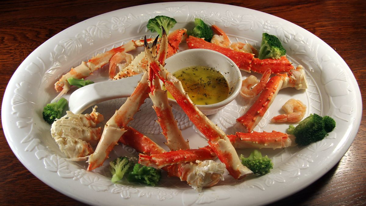 Costco King Crab Legs Served With Butter Sauce and Steamed Broccoli on a White Plate on a Wooden Table