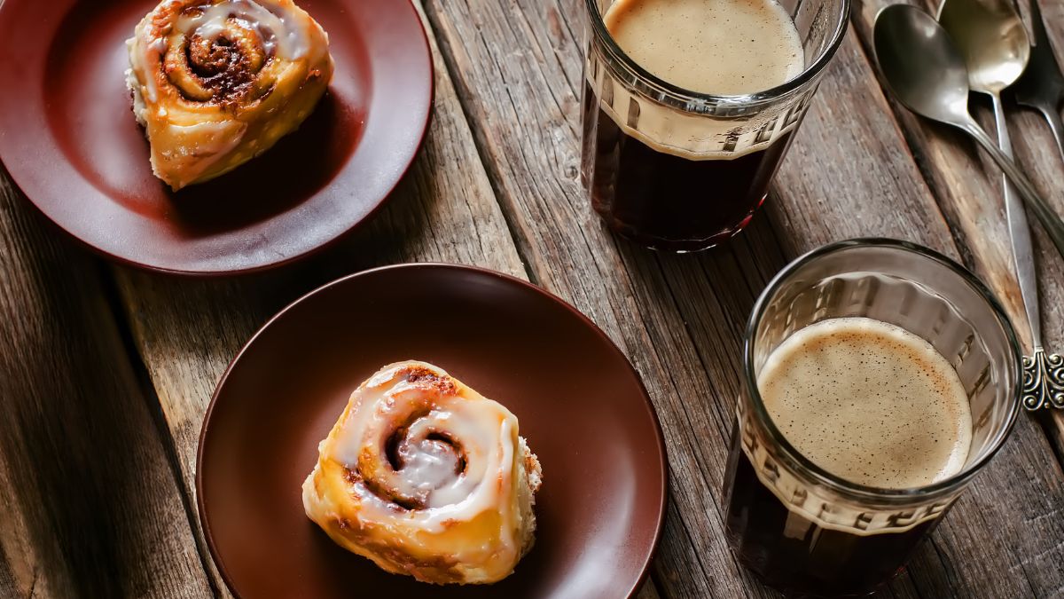 Rhodes Cinnamon Rolls With Vanilla Pudding served on brown plates along with two glass cups of coffee on wooden table
