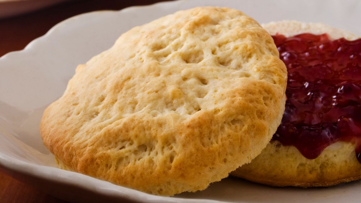 A Pillsbury biscuit cut in half with jam spread over the lower half served on white plate