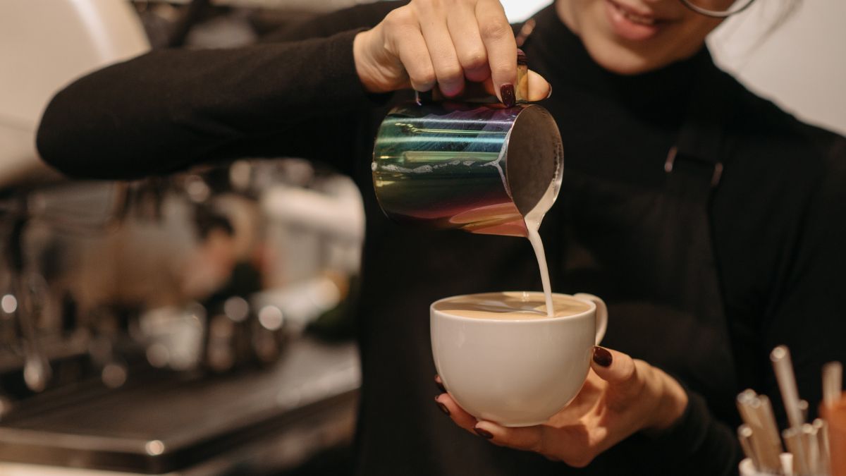 a barista pouring oat milk into a cup of coffee