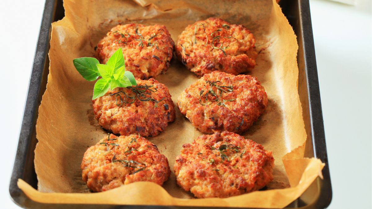 cauliflower patties on a baking-paper-covered baking tray sprinkled with herbs
