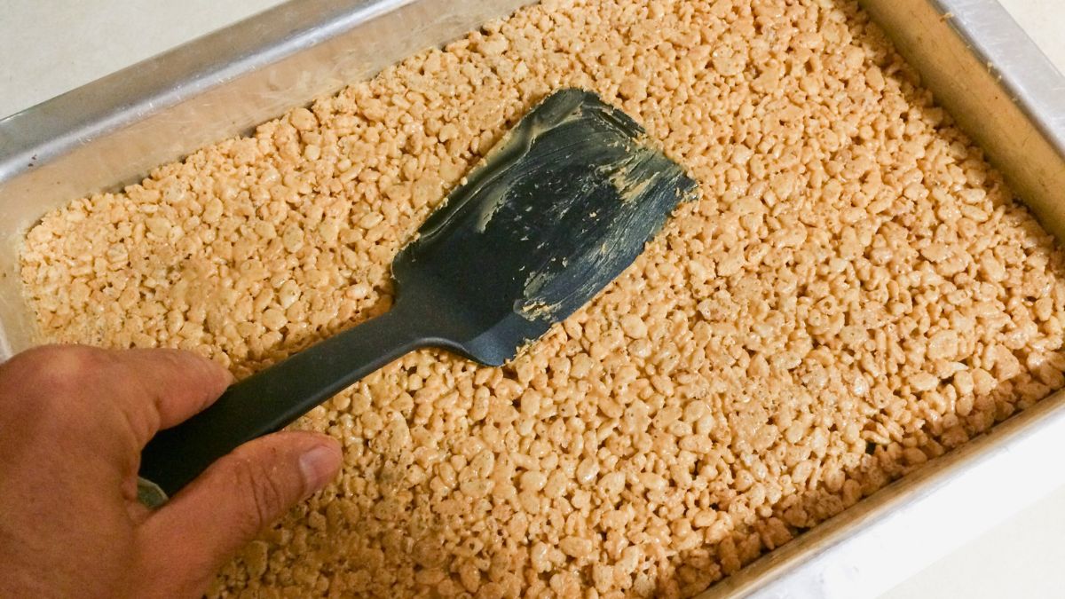 pressing rice krispies with too much butter into a baking tray to put into the freezer