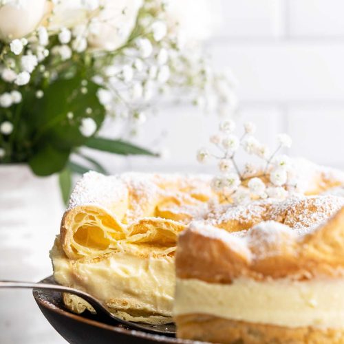 pretty karpatka cake on wooden cake stand with boquet of white roses in background