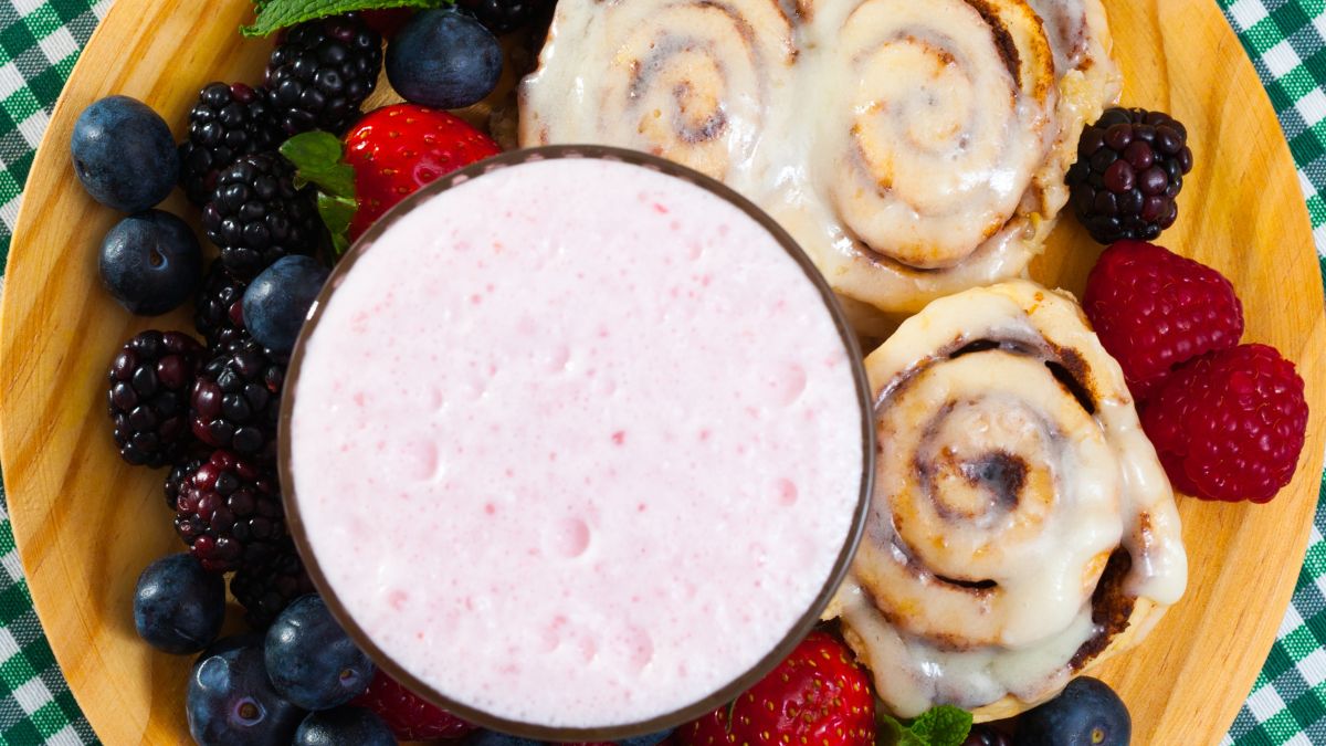 three Rhodes cinnamon rolls served with a berry smoothie on a wooden board decorated with fresh berries